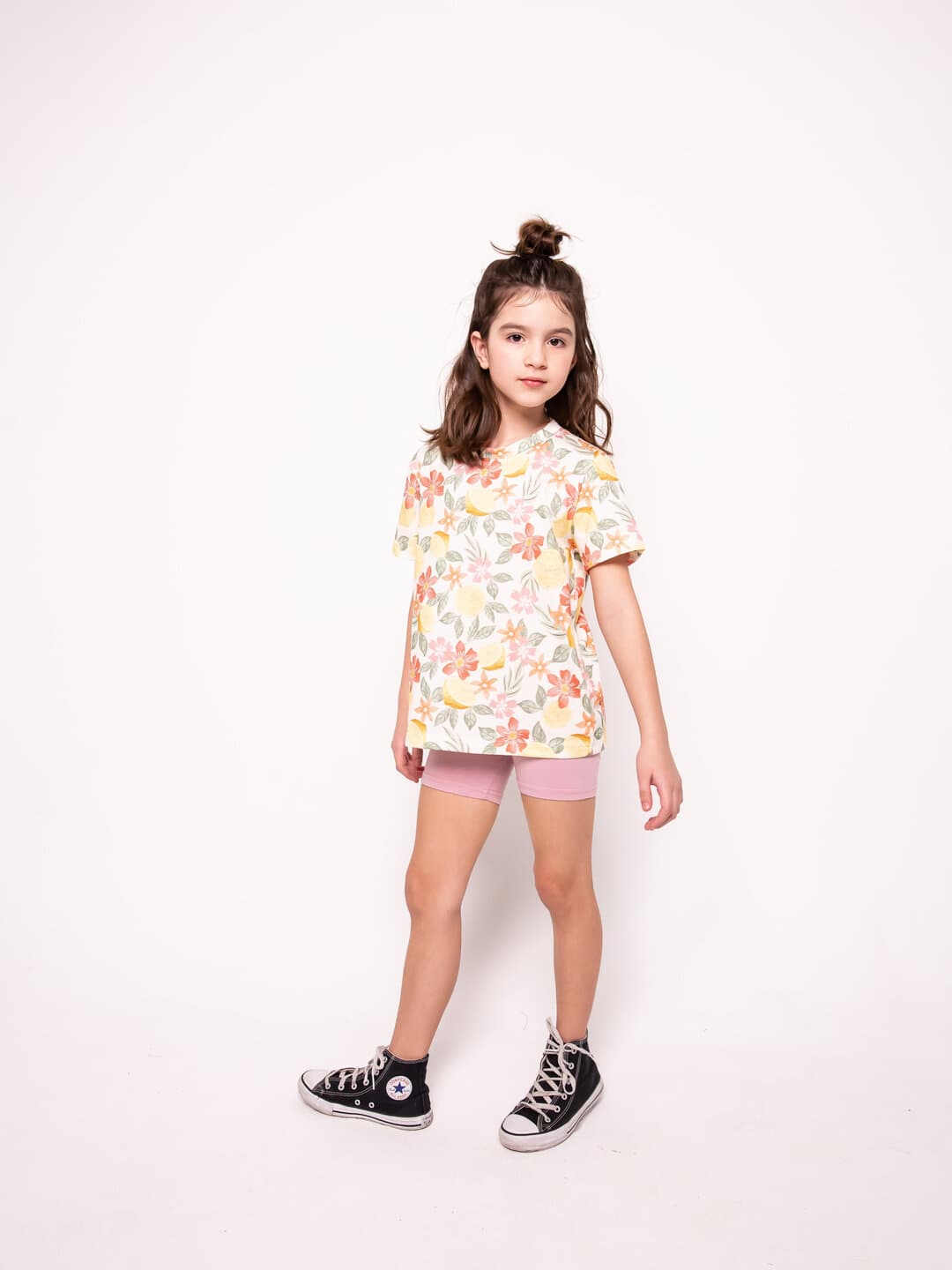 A girl in a floral tee, standing in the studio.