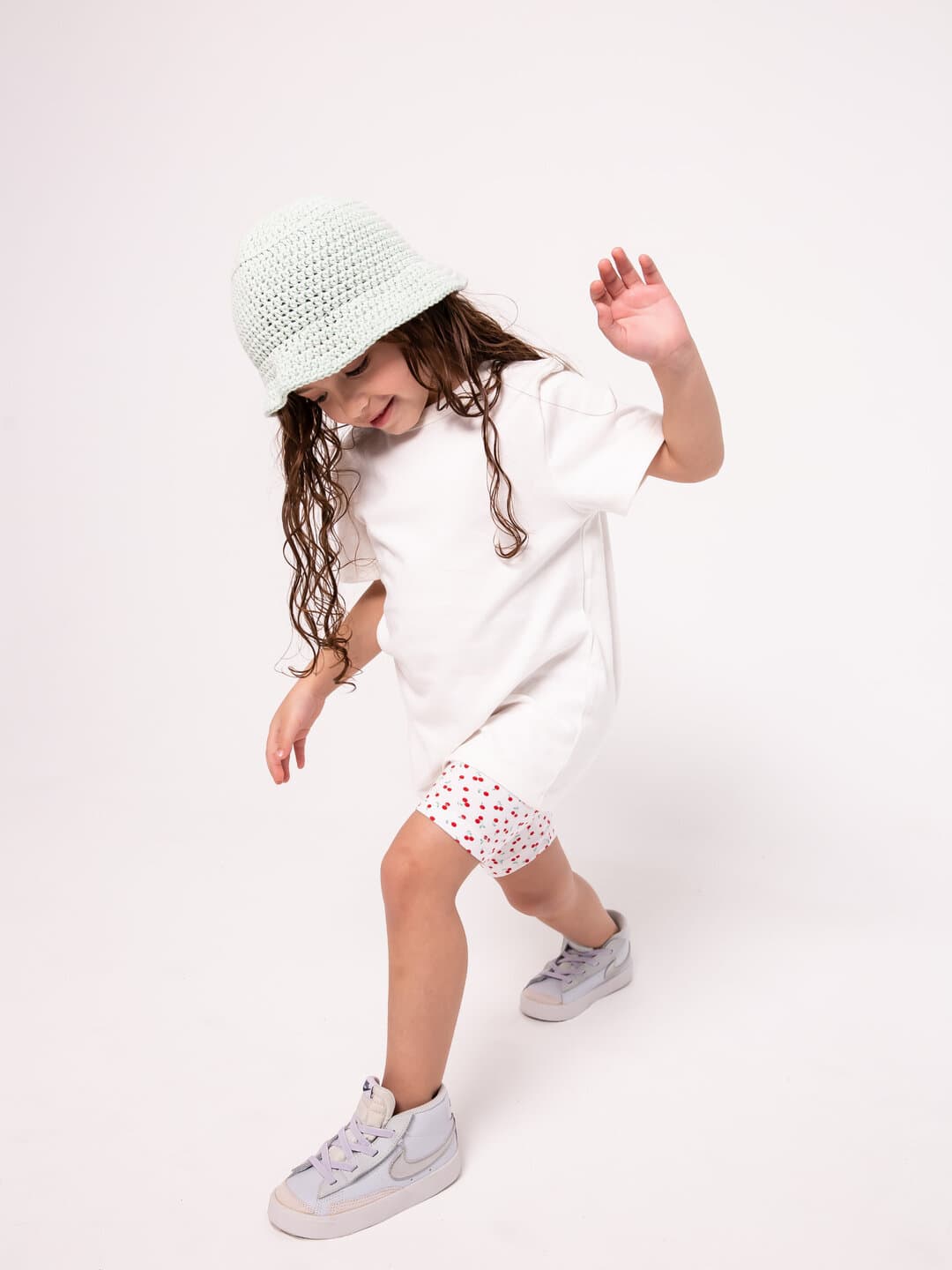A girl in a white tee and a crochet hat, dancing in the studio.